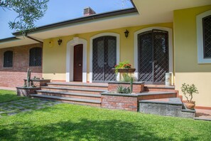Una casa de dos pisos con fachada de ladrillo, un porche con escalones y un pequeño jardín con plantas en macetas.
