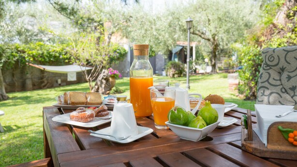 A wooden table set with breakfast items including pastries, a bottle of orange juice, and a bowl of fruit. - Sicily's View (Mascalucia)