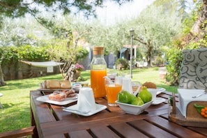 Una mesa de madera con desayuno que incluye bollería, una botella de zumo de naranja y un bol de fruta.