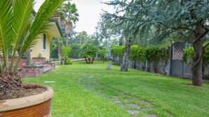 A garden with a pathway, a palm plant, and a brick wall. - Sicily's View (Mascalucia)