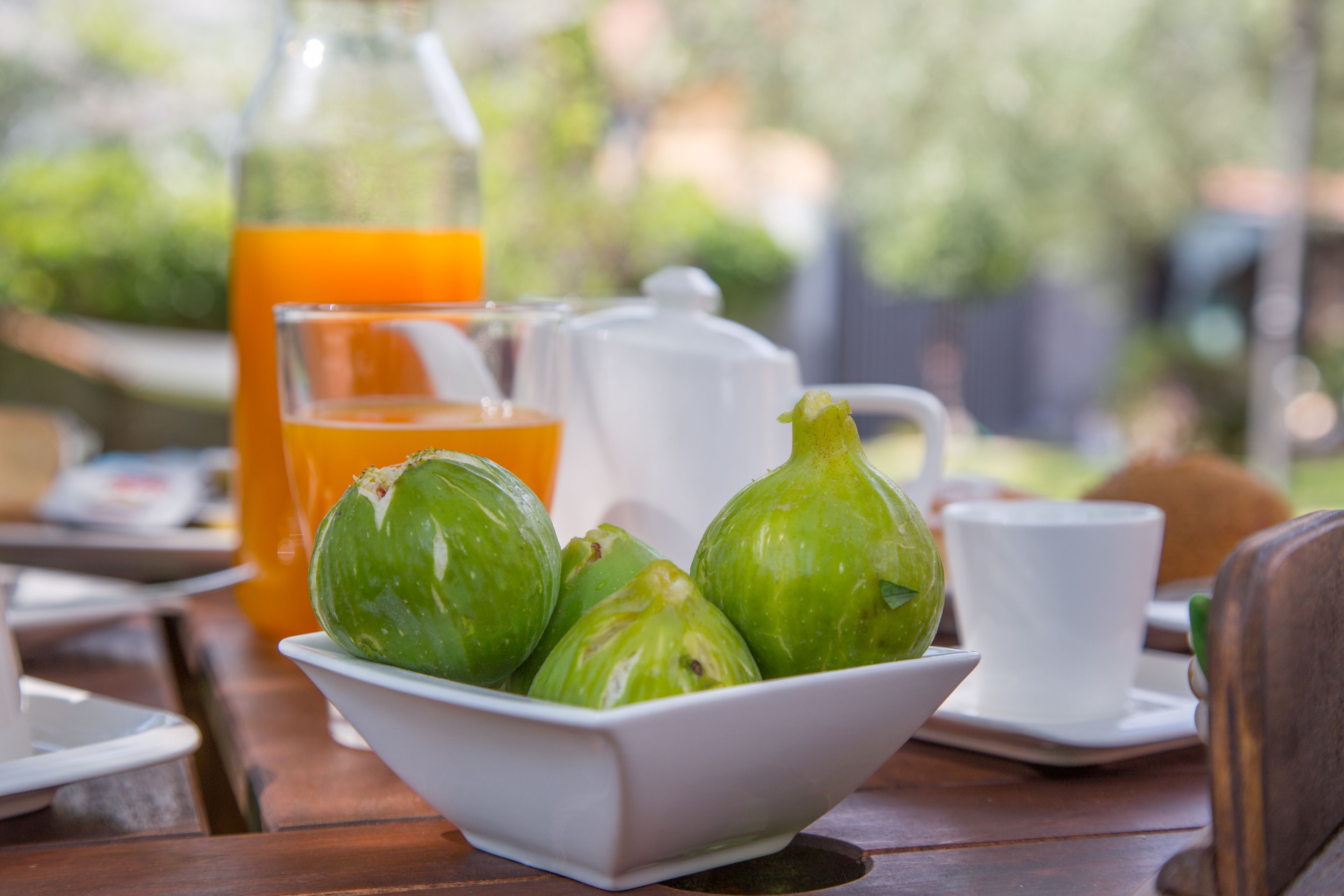 A table with a white bowl containing green fruits, a white cup, and a glass of orange juice.