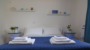 A neatly made bed with a blue quilt, white pillows, and two side tables with folded towels and small vases with flowers. - Sicily's View (Mascalucia)