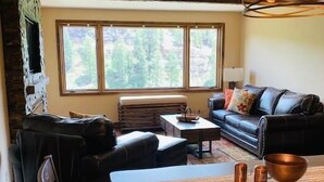 Una sala de estar acogedora con chimenea, un sofá, una mesa de comedor y amplios ventanales con vistas al exterior.