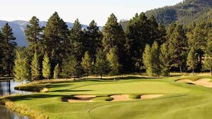 Campo de golf con un estanque, búnkeres de arena y un fondo boscoso.