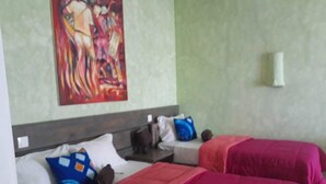 A hotel room with two beds, each with a red bedspread and pillows, a painting on the wall, and a small table with a lamp. - Vivenda Viviani (Praia)