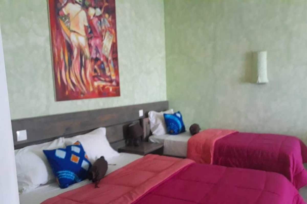Ein Hotelzimmer mit zwei Betten, jeweils mit roter Bettdecke und Kissen, einem Gemälde an der Wand und einem kleinen Tisch mit Lampe.