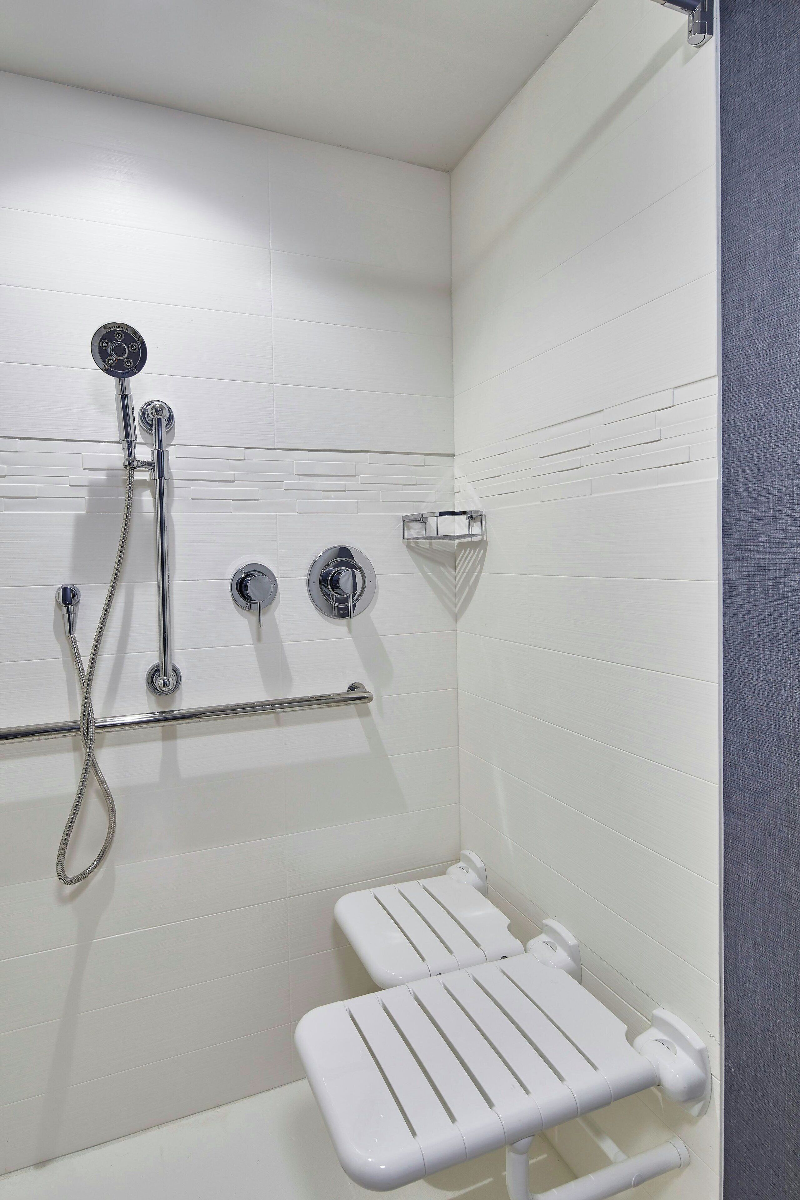 A modern bathroom with white tiled walls, a shower with chrome fixtures, and a white grab bar.