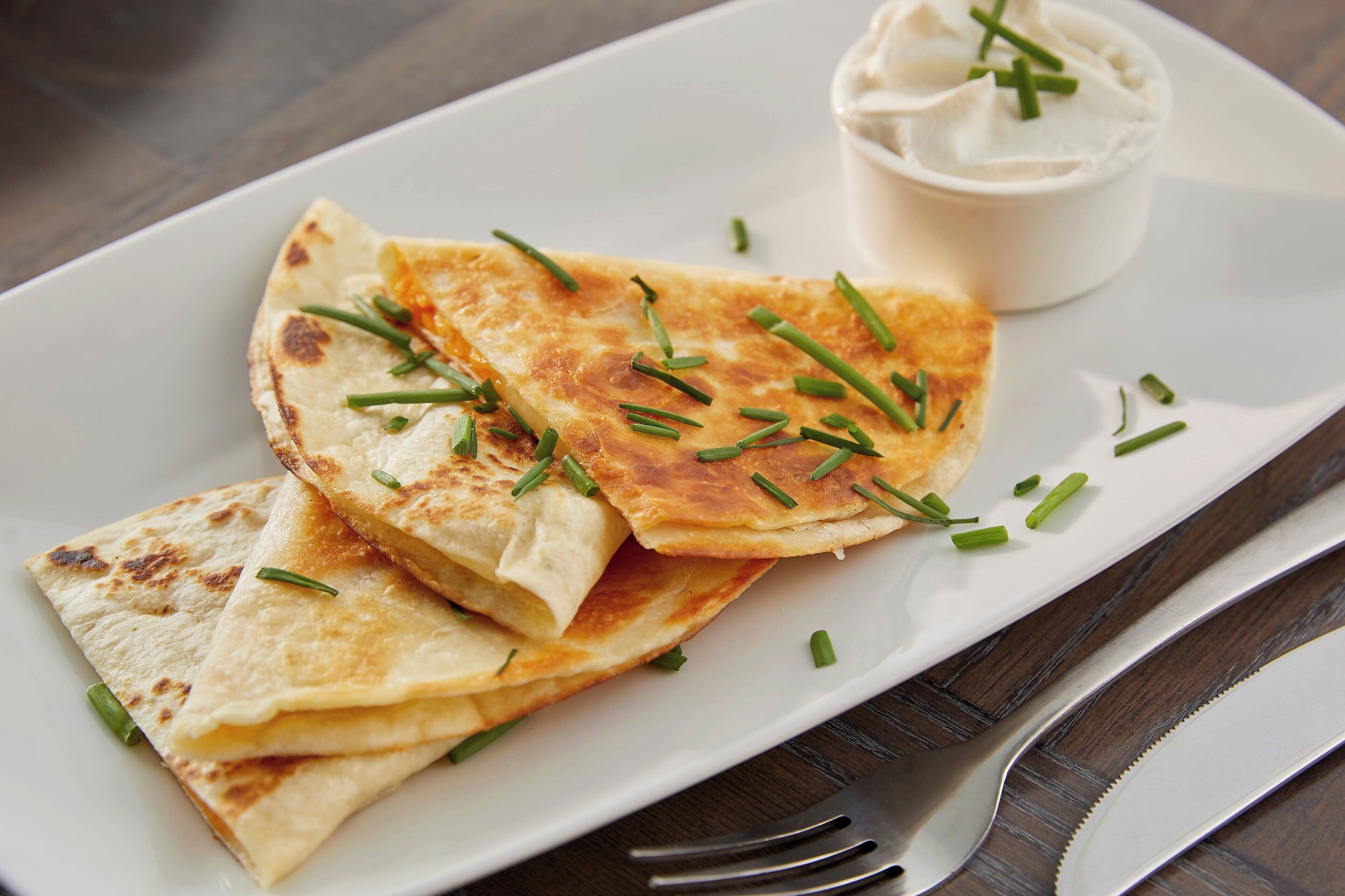 A plate of quesadillas garnished with chives, accompanied by a small bowl of sour cream.
