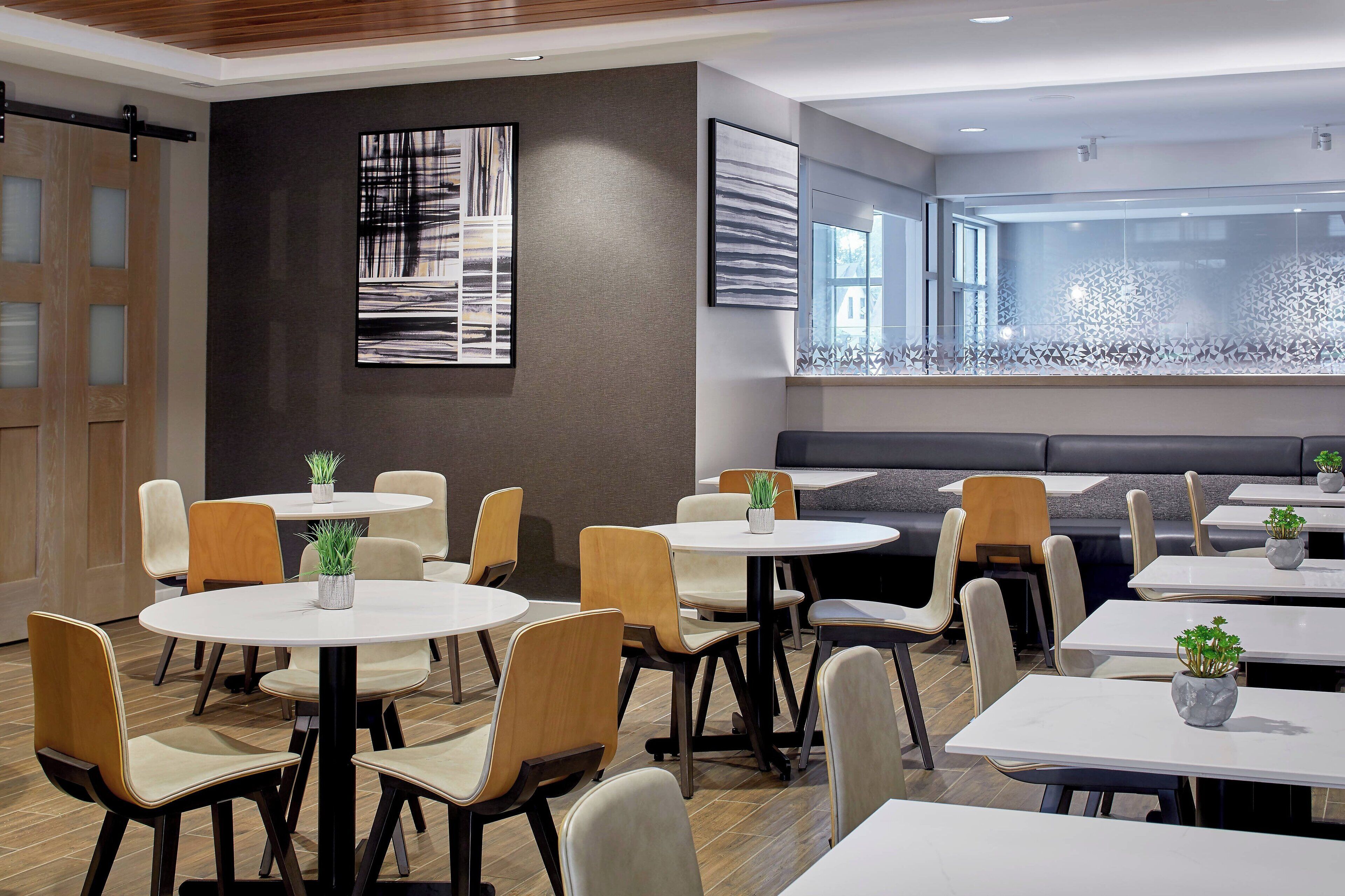 A modern dining area with round tables and chairs, a large window with a view, and abstract art on the walls.