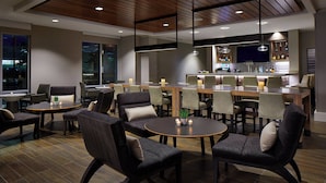 A modern lounge area with round tables and comfortable seating, a bar with a large screen, and a view of the city at night. - Residence Inn by Marriott Cleveland University Circle/Medical Center (Cleveland)