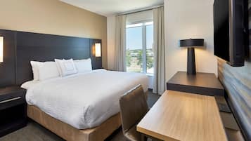 A hotel room with a large bed, a desk, a television, and a view of the city.