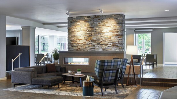 A modern living room with a stone fireplace, comfortable seating, and a large window offering a view of the outdoors. - Residence Inn by Marriott Cleveland University Circle/Medical Center (Cleveland)