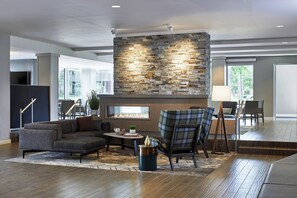 A modern living room with a stone fireplace, comfortable seating, and a large window offering a view of the outdoors. - Residence Inn by Marriott Cleveland University Circle/Medical Center (Cleveland)