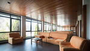 A spacious room with a large sofa set, a coffee table, and a window with blinds. - HI Sao Pedro do Sul Pousada de Juventude - Hostel (Sao Pedro do Sul)