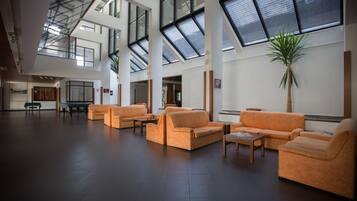 A spacious lobby with high ceilings, large windows, and orange sofas arranged for seating.