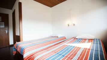 A room with two beds, wooden ceiling beams, white walls, and a door.