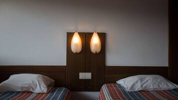A hotel room with two beds, each with a striped bedspread and white pillows. There are wall-mounted lights above the beds.
