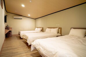 Ein Hotelzimmer mit drei Betten, Holzboden, einer Klimaanlage und einer kleinen Ablage mit Gegenständen.