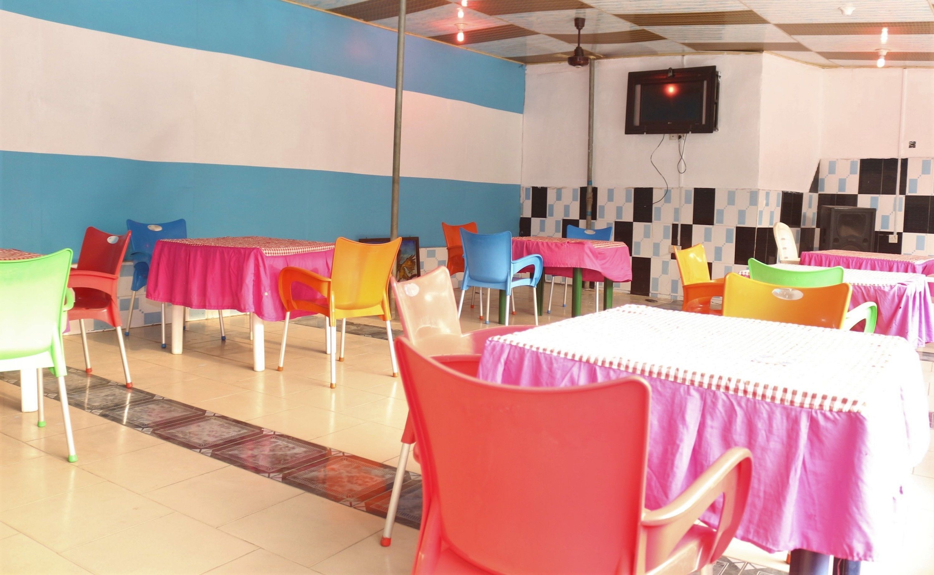 A dining area with multiple tables and chairs, a television mounted on the wall, and a tiled floor.