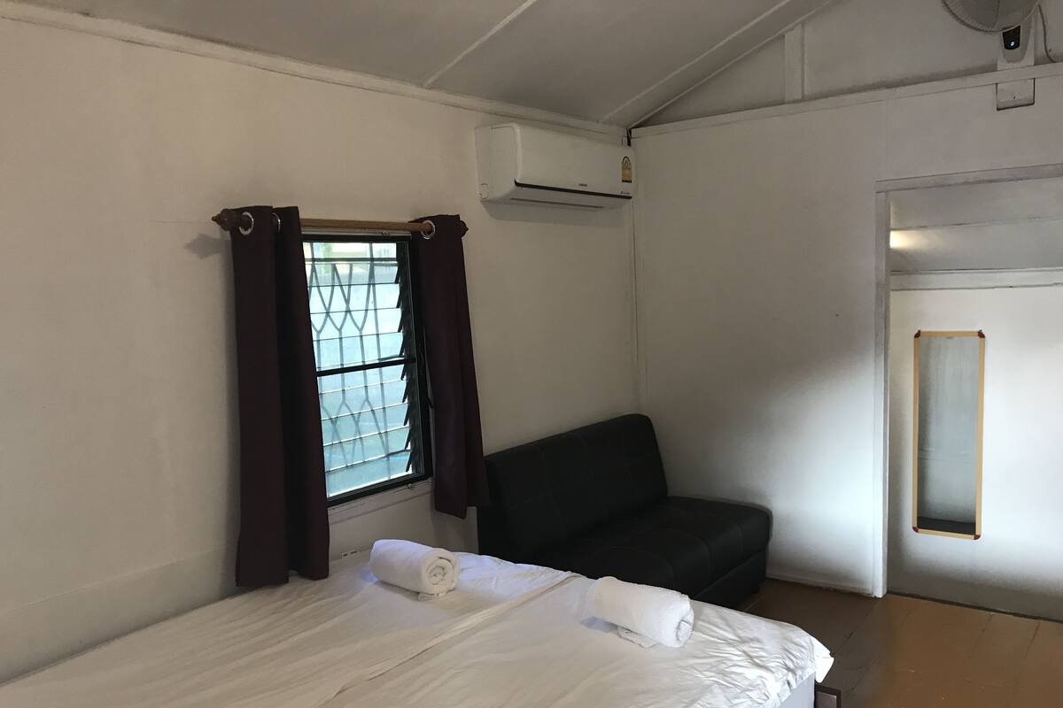 Quarto com cama, janela com cortinas, sofá preto e ar condicionado.