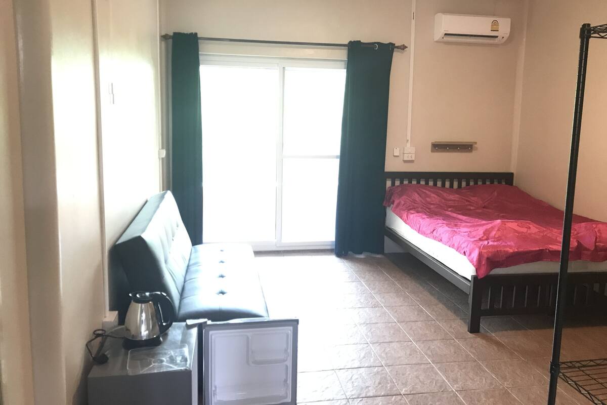 Quarto com cama, escrivaninha, cadeira e janela com cortinas.