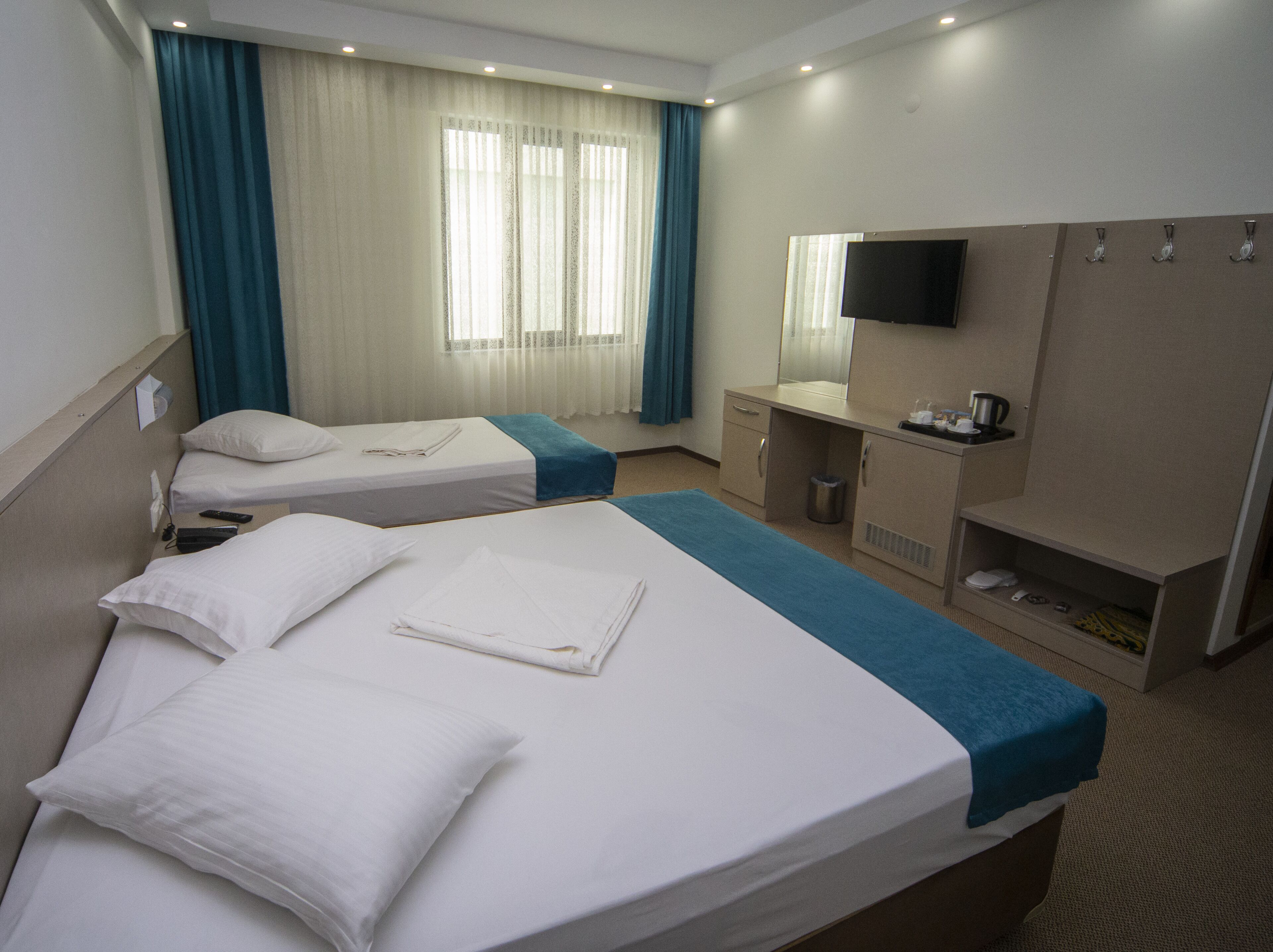 Habitación de hotel con dos camas individuales, un escritorio, un espejo, un televisor y una ventana con cortinas.