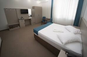 Ein Hotelzimmer mit einem Bett, einem Schreibtisch, einem Stuhl, einem Fernseher und einem Kleiderschrank.