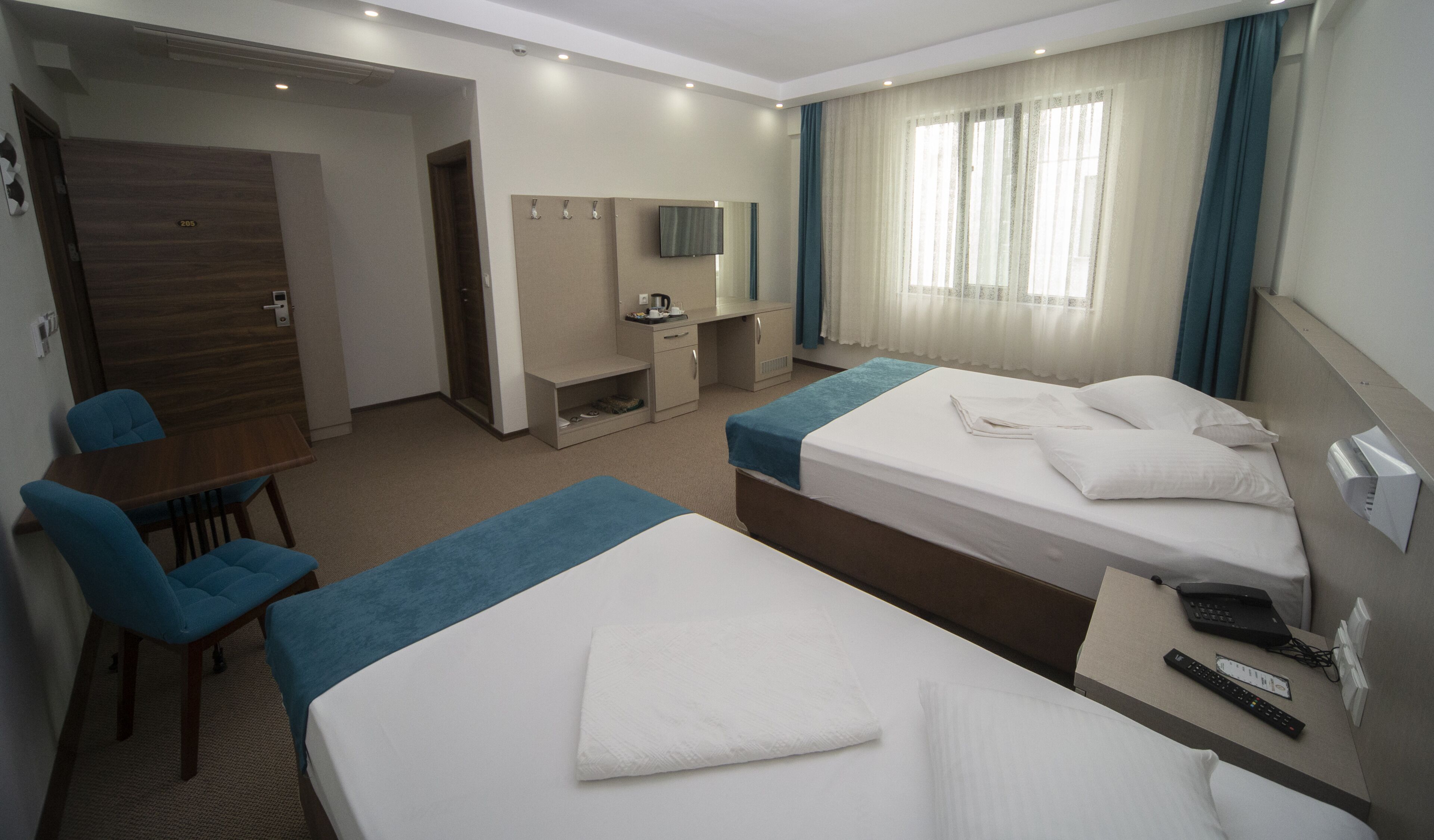 A hotel room with two beds, a desk, a chair, a TV, and a window with curtains.