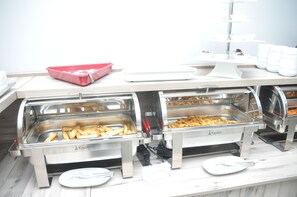 Ein Buffet mit mehreren Edelstahl-Serviertabletts, beschriftet mit 'Kayalar', belegt mit verschiedenen Speisen wie Pommes und möglicherweise anderen Snacks.