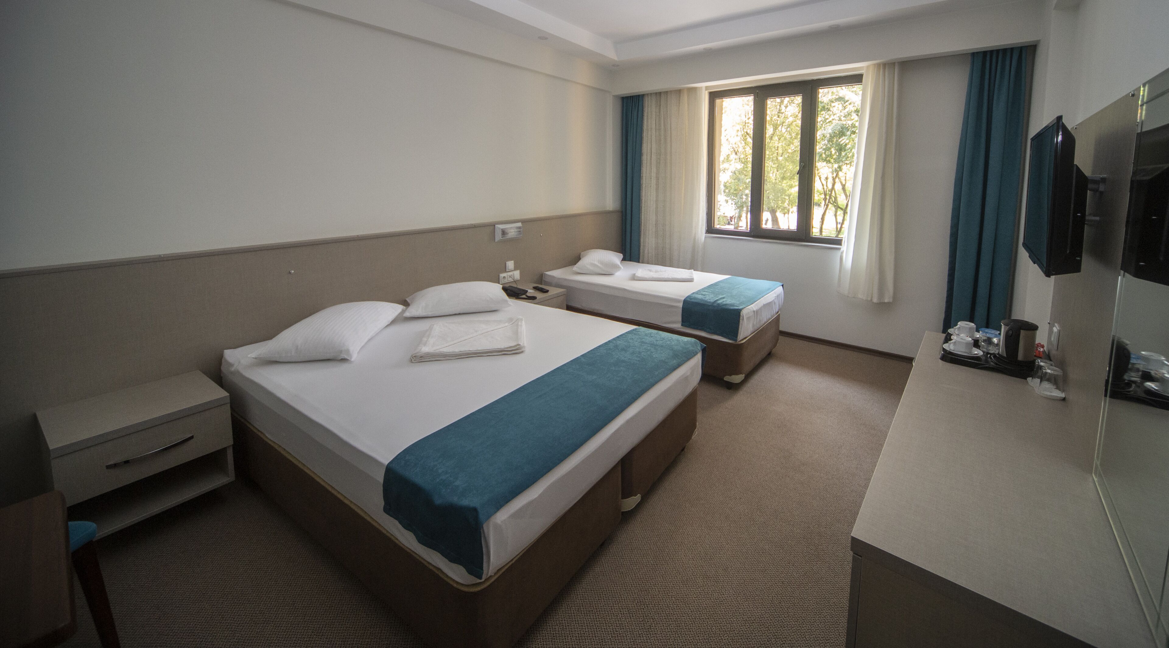Habitación de hotel con dos camas, un escritorio, una silla, un televisor y una ventana con cortinas.