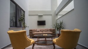 Una sala de estar moderna con un sofá color beige, dos sillones amarillos, una mesa de centro y un televisor en la pared.