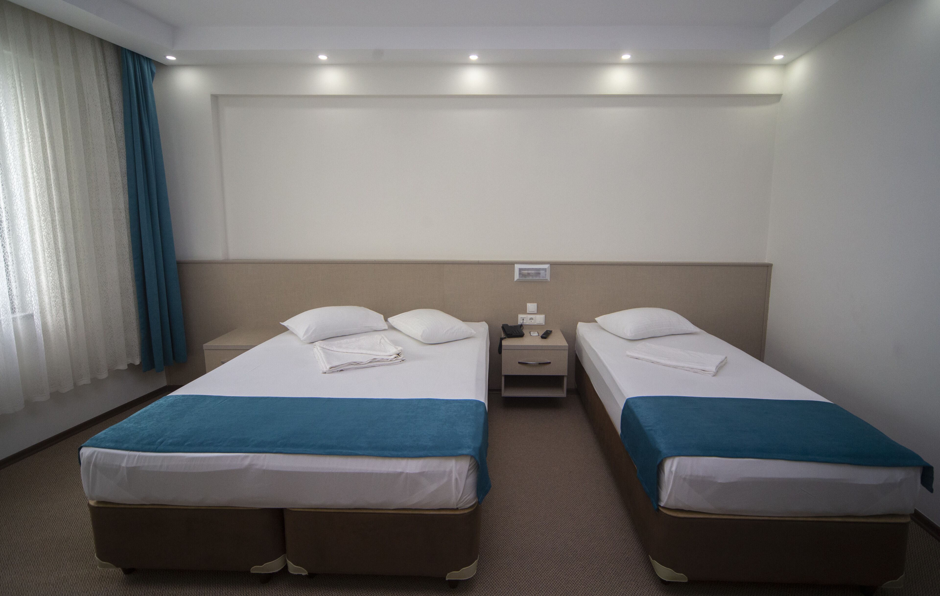 A hotel room with two beds, a nightstand, and a window with curtains.
