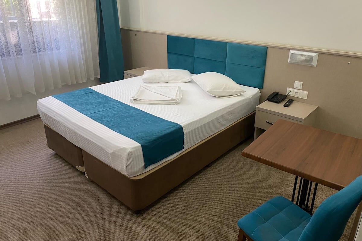 Une chambre d’hôtel comprenant un lit, une table de chevet avec un téléphone et une télécommande, une petite table et une chaise.