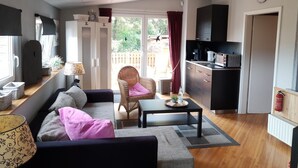 A cozy living room with a sofa, a wicker chair, a coffee table, and a kitchen area with cabinets and a microwave. - Gasthaus Düther Schleuse (Fresenburg)