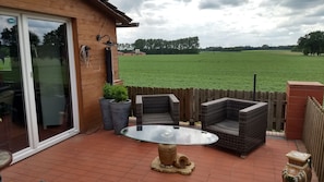 A patio with two wicker chairs and a glass table, a wooden fence, and a view of a green field. - Gasthaus Düther Schleuse (Fresenburg)