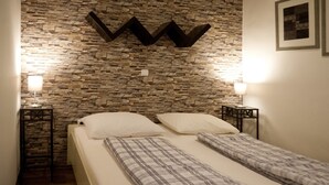 A bedroom with a stone wall, two beds, bedside lamps, and a framed picture. - Gasthaus Düther Schleuse (Fresenburg)