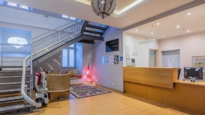 A hotel reception area with a reception desk, a staircase, and a wall-mounted television.
