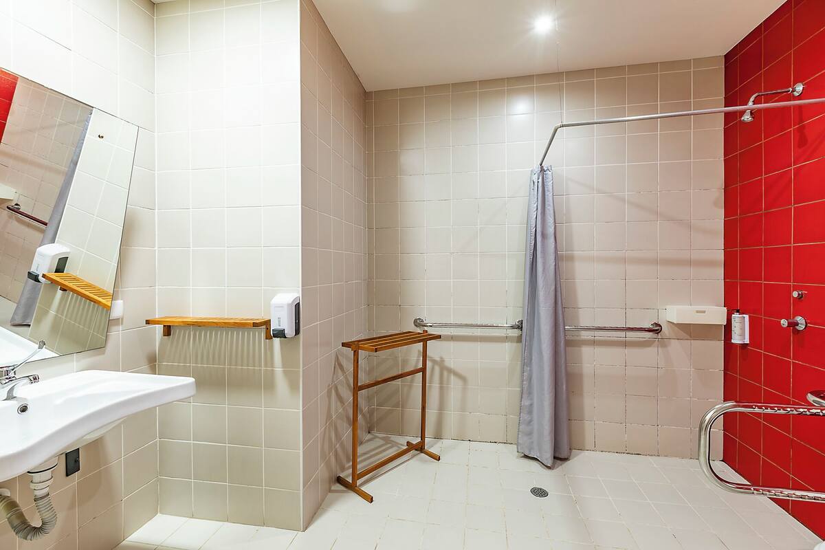Ein Badezimmer mit Waschbecken, Spiegel, Handtuchhalter, Dusche und einer roten Akzentwand.