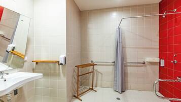 A bathroom with a sink, mirror, towel rack, shower, and a red accent wall.