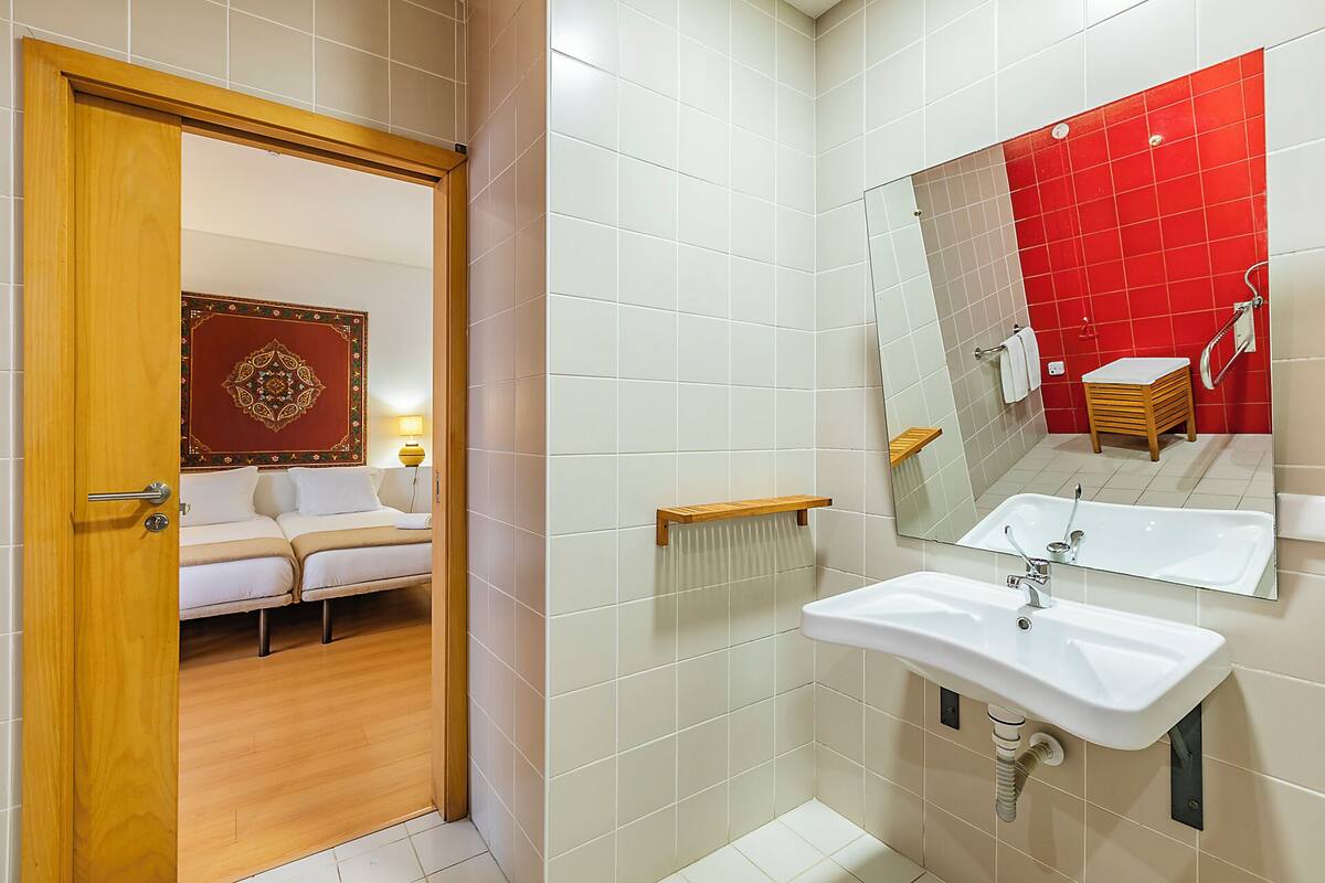 Ein Hotelbad mit einem großen Spiegel, einem weißen Waschbecken und einer roten Akzentwand.
