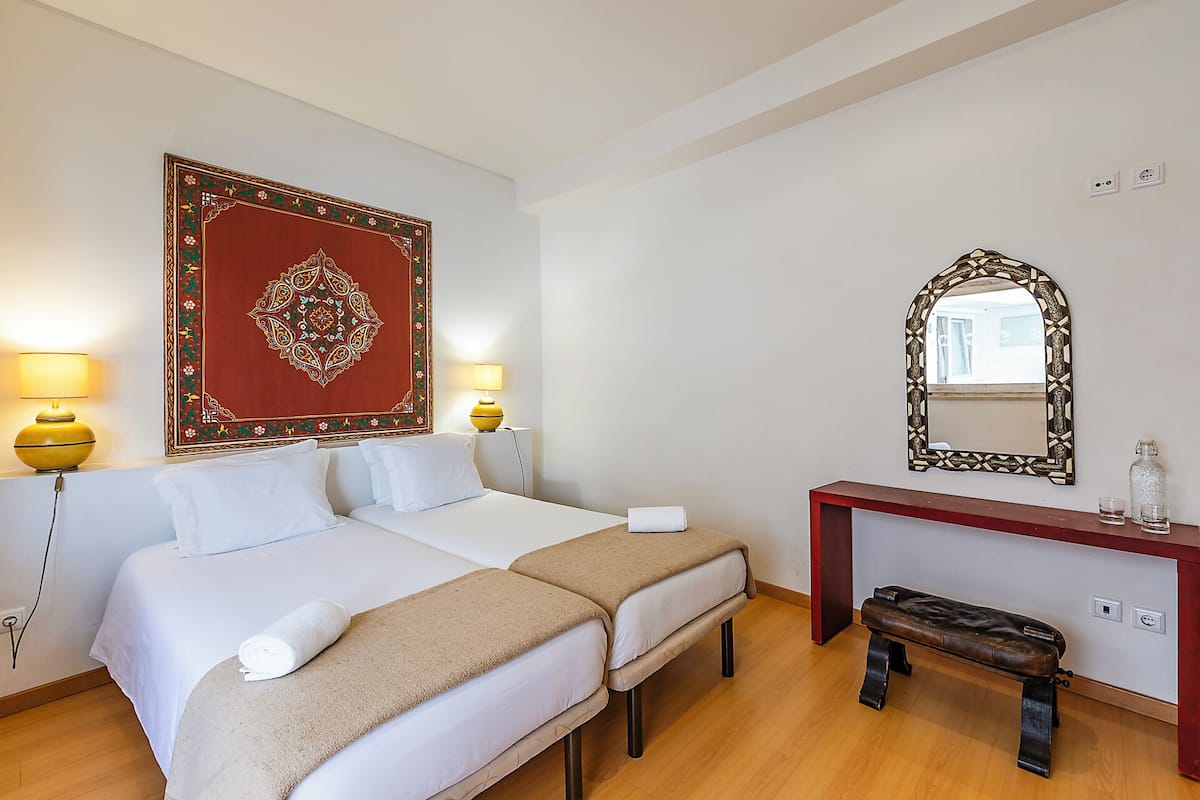 Ein Hotelzimmer mit zwei Betten, einer Holzbank, einem Konsolentisch mit Spiegel und Wanddekoration.