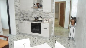 Uma cozinha compacta com armários brancos, fogão a gás e pia. Há uma área de refeições com mesa e cadeiras.