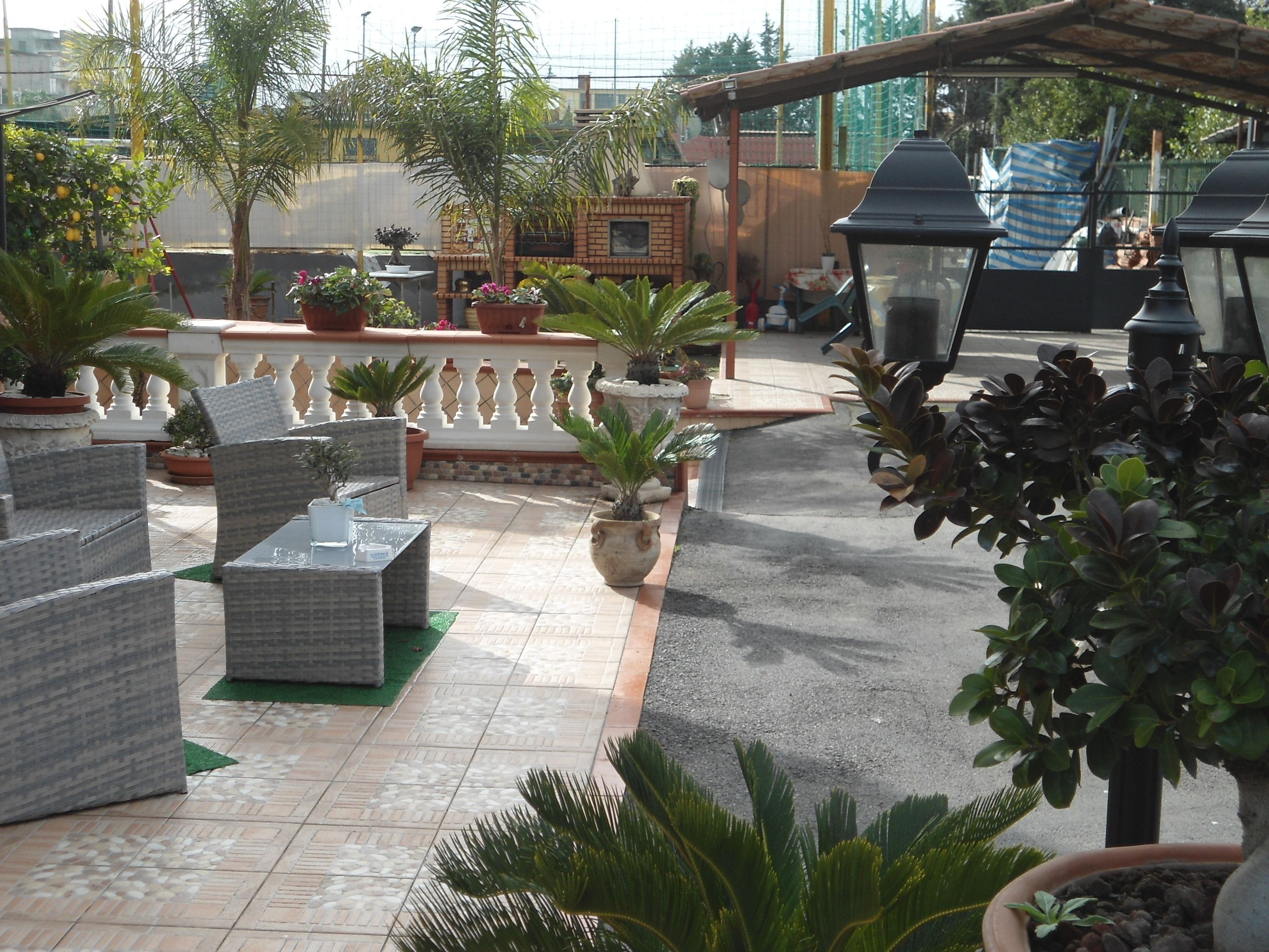Un espacio al aire libre con patio, muebles de mimbre, plantas en macetas y una parrilla.