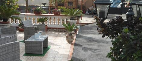 Un espacio al aire libre con patio, muebles de mimbre, plantas en macetas y una parrilla.