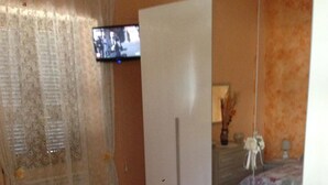 Quarto com uma cama, guarda-roupa, televisão e espelho.