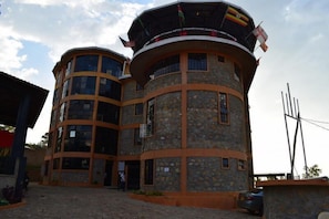 A multi-story building with a stone facade, multiple balconies, and flags. - Kibar Mos Hotel and Lodges (Chwele)