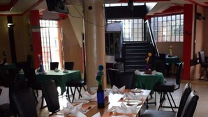 A dining area with tables set for four, black chairs, and a staircase in the background.