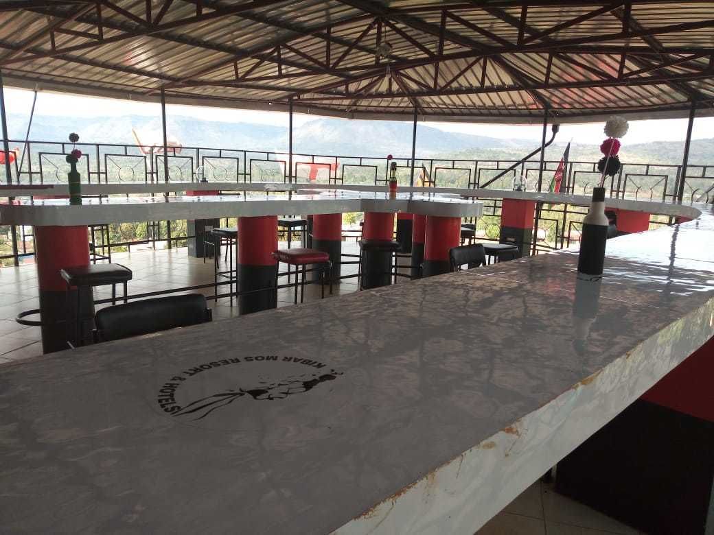 Ein Restaurant mit einer langen Theke, roten und schwarzen Stühlen und Blick auf Berge.