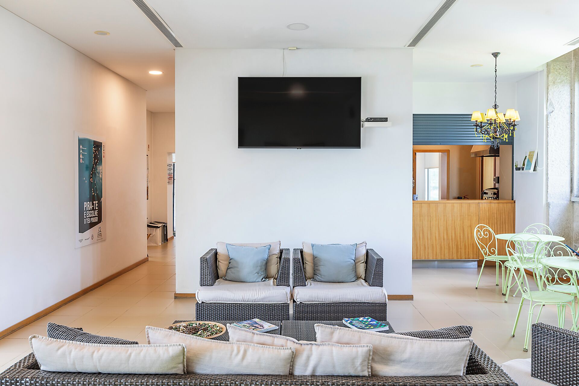 Uma sala de estar com televisão de tela plana, móveis de vime e uma área de jantar com cadeiras verdes.
