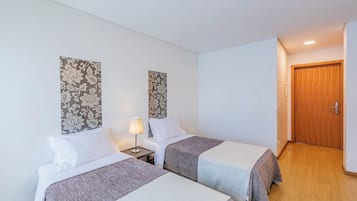 Una habitació d'hotel amb dos llits, una taula de nit amb una làmpada, una porta de fusta i paper pintat amb motius florals.